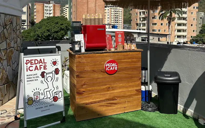 Barra de café móvil de PEDALiCAFÉ con máquina de espresso roja, montada en una azotea bajo una sombrilla de paja